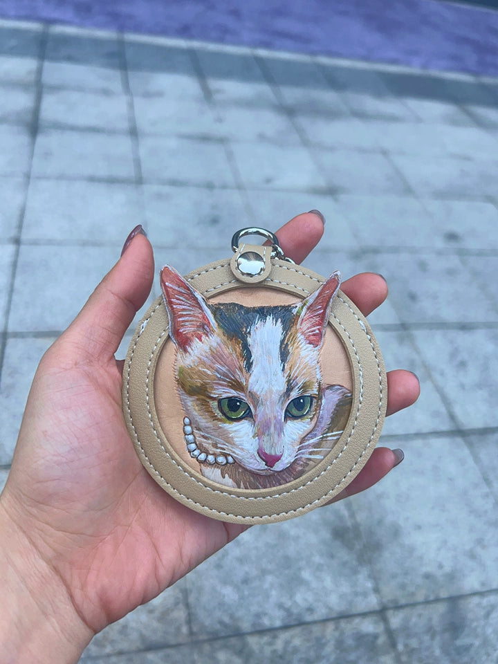 Calico cat portrait on almond leather keychain held up outdoors